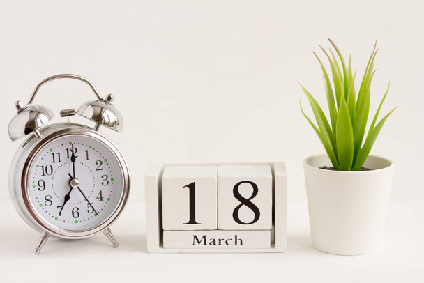 March 18 on a wooden calendar next to an alarm clock and a flower on a white background. The concept of one day a year.Significant date or event - Foto, Bild