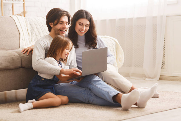 Ευτυχισμένη οικογένεια με την κόρη χρησιμοποιώντας φορητό υπολογιστή μαζί στο σπίτι - Φωτογραφία, εικόνα