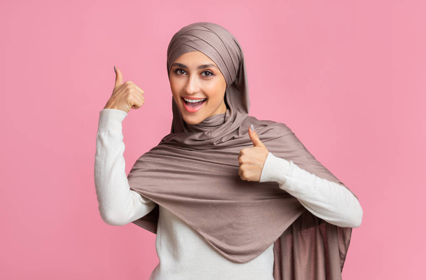felice musulmano ragazza in hijab gesturing pollice su con entrambe le mani
 - Foto, immagini