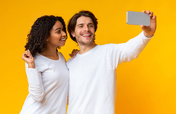 Cheerful interracial couple taking sellfie on smartphone together - Fotó, kép