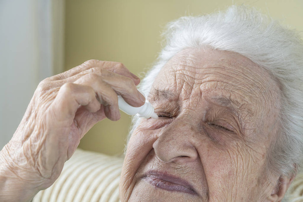 a senior woman applying eyedrops into her eyes by herself - Foto, imagen