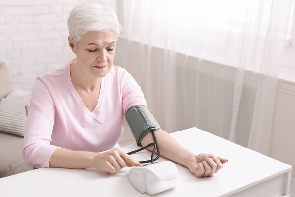 Senior lady with hypertension measuring blood pressure herself - Foto, afbeelding