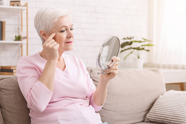 Elderly woman looking for wrinkles around eyes at home - Фото, зображення