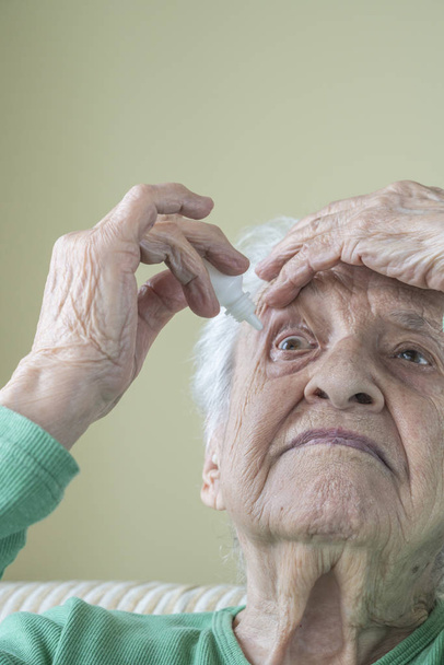 a senior woman applying eyedrops into her eyes by herself - Photo, Image