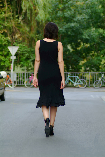 Μια γυναίκα με μαύρο φόρεμα κάνει μια βόλτα στην πόλη. - Φωτογραφία, εικόνα