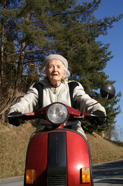 senior woman in red riding scooter on a motorcycle - Zdjęcie, obraz