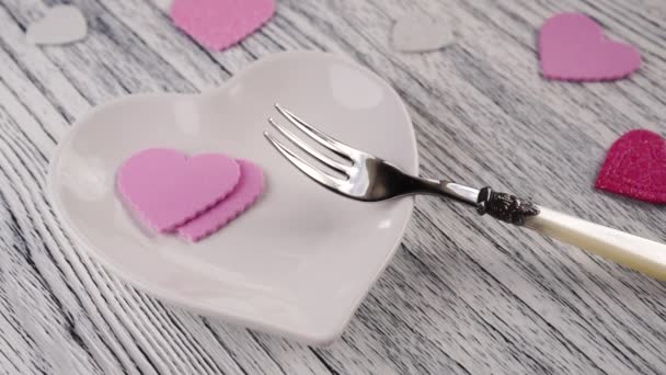 Decorative hearts fall on a heart-shaped plate with a dessert fork. On a wooden light texture table. Pink red and white. Happy Valentine's Day Greetings - Imágenes, Vídeo