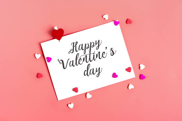 愛する人へのメッセージのための白い紙、ピンクの背景にハートの形をした赤い封筒とキャンディー。ハッピーバレンタインデーのコンセプトテキストのためのフラットレイモックアップ場所トップ表示  - 写真・画像