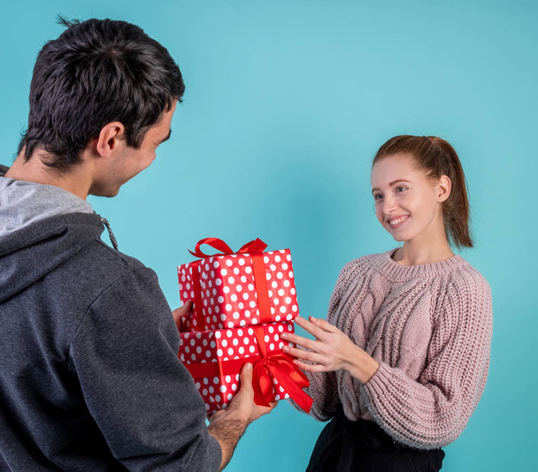 Young smiling woman accepting gifts from her boyfriend isolated on blue background - Photo, Image