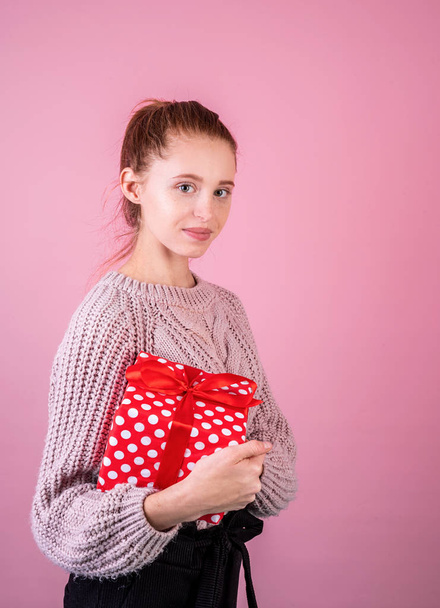 Приваблива молода блондинка тримає червону подарункову коробку на рожевому фоні
 - Фото, зображення