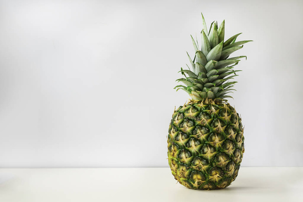 un intero ananas maturo si erge su una superficie bianca con uno sfondo grigio chiaro. - Foto, immagini