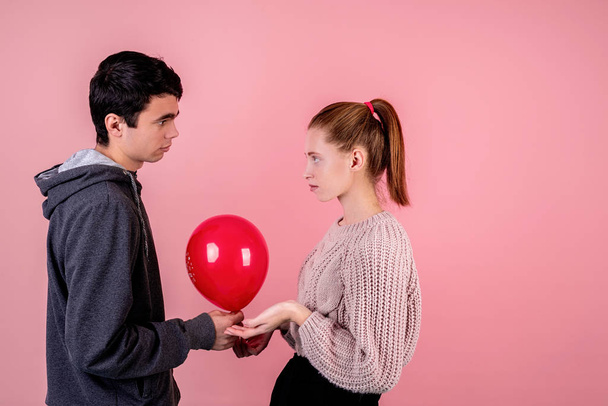 casal infeliz olhando uns para os outros segurando um balão vermelho isolado no fundo rosa
 - Foto, Imagem