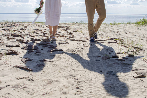 νεόνυμφοι περπατούν στην παραλία, με ένα γαμήλιο μπουκέτο στα χέρια τους - Φωτογραφία, εικόνα