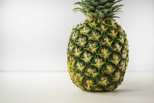 a whole ripe pineapple stands on a white surface with a light gray background. - Zdjęcie, obraz