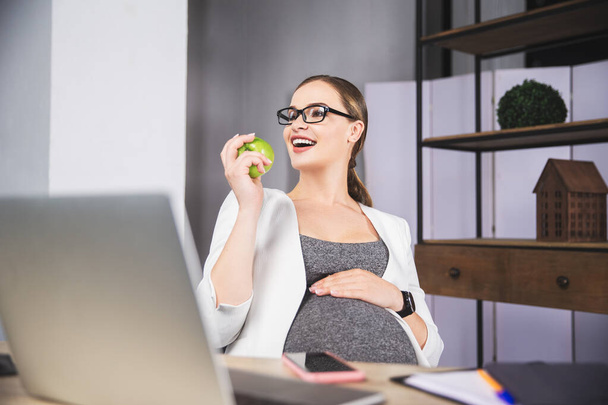 Jovem grávida segurando maçã no escritório
 - Foto, Imagem