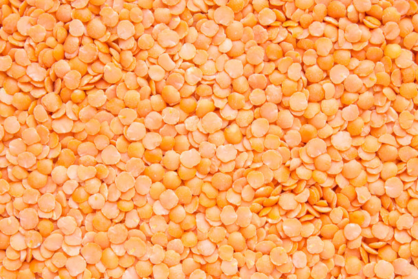 Unfocused orange lentil completely scattered in an even layer on a flat surface. Natural close-up background with copy space - Foto, afbeelding