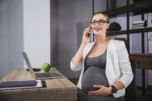 Беременная деловая женщина, работающая в офисе, сидящая на телефоне
 - Фото, изображение