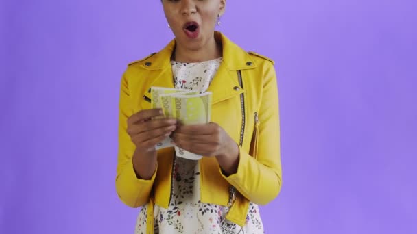 Attractive Afro american woman is counting money against a purple background Yellow jacket - Filmati, video