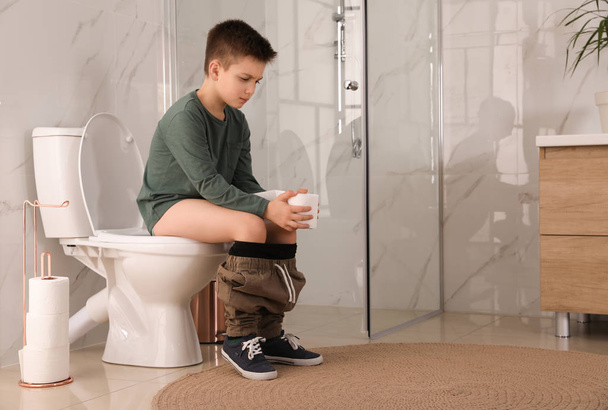 Boy with paper suffering from hemorrhoid on toilet bowl in rest room - Zdjęcie, obraz