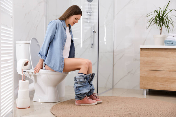 Woman suffering from hemorrhoid on toilet bowl in rest room - 写真・画像