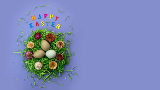 Paascompositie met nest, eieren en kleurrijke letters op violette achtergrond. Tekst Vrolijk Pasen. - Foto, afbeelding
