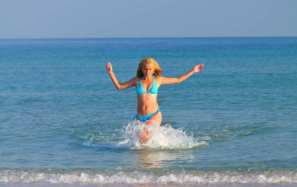 Young woman in sportswear running near still sea edge and smiling - Foto, imagen