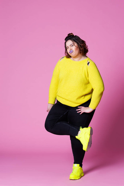 Cheerful plus size model in casual clothes, fat woman in black jeans and yellow jumper on pink background - Foto, Imagem