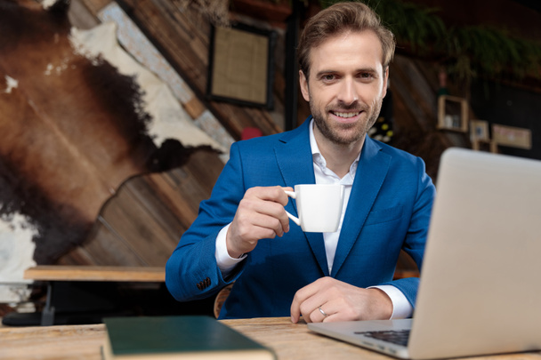 Positiivinen liikemies hymyilee ja pitelee kahvia.
 - Valokuva, kuva