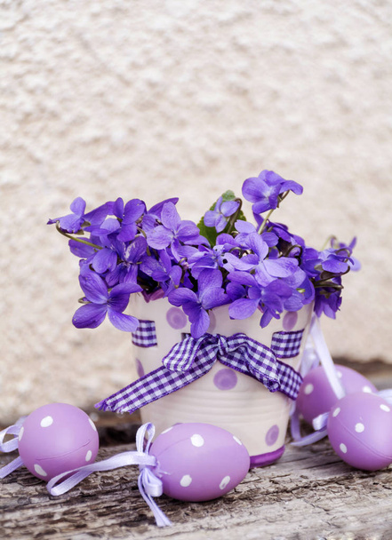 white dotted pot with purple flowers and Easter eggs on wooden table background  - Φωτογραφία, εικόνα