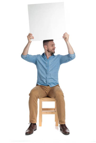 young casual man holding empty board above head - Photo, Image