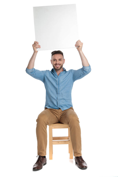 happy casual man holding empty board above head - Foto, Imagen