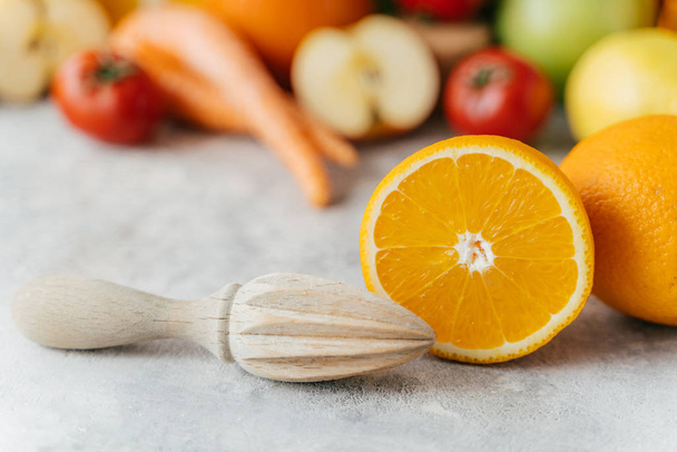 Plaszony pomarańczowy i drewniany wyciskarki na tle niewyraźne owoce i warzywa tła. Wyciśnięte świeże owoce cytrusowe. Koncepcja zdrowego odżywiania - Zdjęcie, obraz