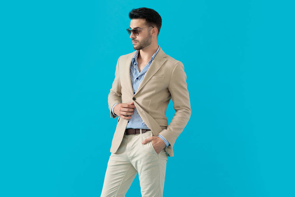 confident young man wearing sunglasses and adjusting coat - Zdjęcie, obraz