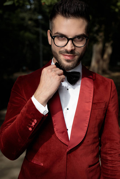 businessman wearing red tuxedo and eyeglasses fixing bowtie - Фото, изображение