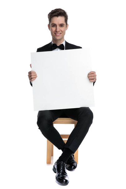 šťastný mladý muž drží prázdnou desku a usmívá se - Fotografie, Obrázek