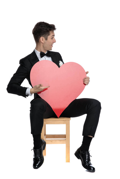 gelukkig jong elegant man presenteren naar kant groot rood hart  - Foto, afbeelding