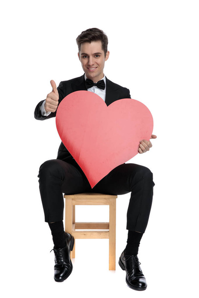 happy young guy holding big red heart and making thumbs up sign - Zdjęcie, obraz