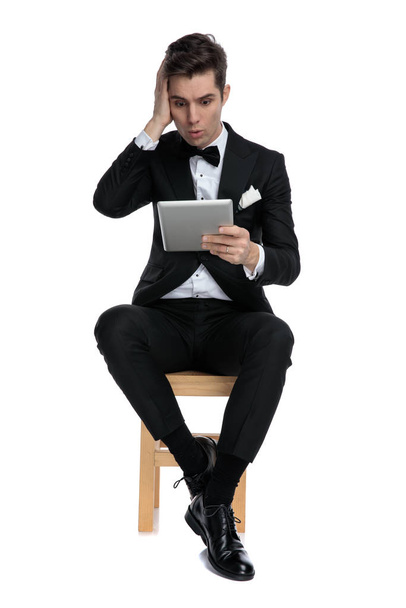 shocked young elegant man holding tab and touching head - Photo, Image