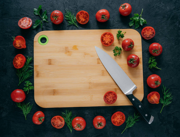 Horizontal top view of red tomatoes lying around wooden chopping board. Green parsley and dill. Knife near. Vegan table. Food concept - Fotografie, Obrázek