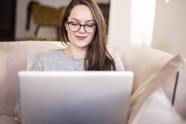 Lähikuva kuva hymyilevä nainen käyttää kannettavaa tietokonetta, kun istuu nojatuolissa kotona. Pääkonttori
.  - Valokuva, kuva