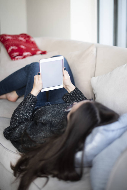 Знімок заднього виду жінки, що лежить на дивані вдома і тримає цифровий планшет порожній екран в руках
. - Фото, зображення