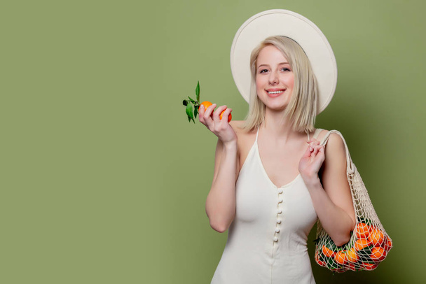 Hermosa mujer con sombrero y vestido blanco con mandarinas
 - Foto, imagen
