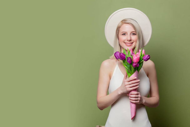Mooi blond meisje met witte hoed en jurk met tulpen - Foto, afbeelding