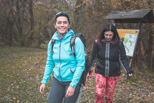 Two female hikers walking, road map behind them. Hiking, outdoor activity - Valokuva, kuva