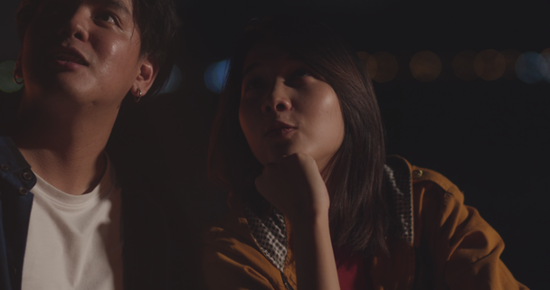 Young asia couple backpackers looking sky in camping at night near campfire on beach. Male and female traveler relax and talking at campsite. Outdoor activity, adventure travel, or holiday vacation. - Materiał filmowy, wideo