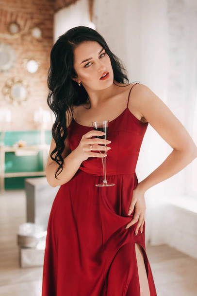 Beautiful woman in red dress with glass of champagne near Christmas tree   - Фото, изображение