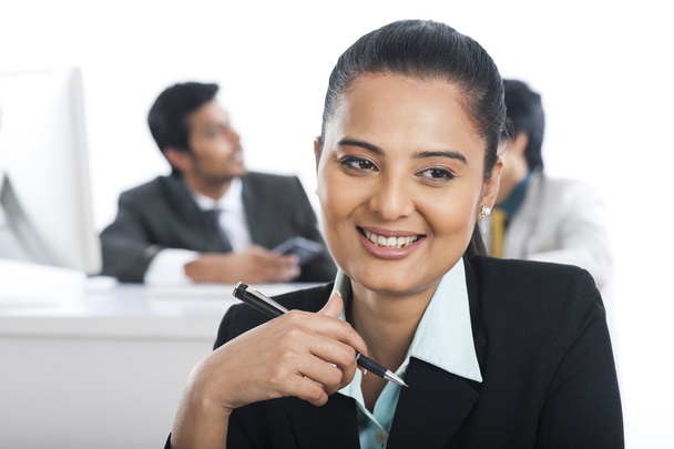 Деловая женщина улыбается в офисе со своими коллегами на заднем плане
 - Фото, изображение