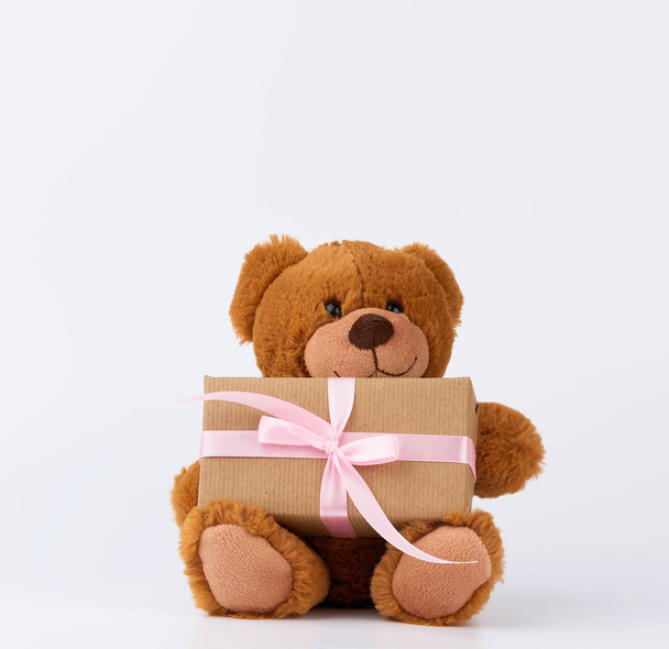 Niedlichen kleinen braunen Teddybär hält eine braune Schachtel mit einem rosafarbenen Band - Foto, Bild