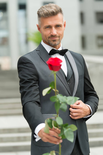 his look very fashion-forward. groom in costume and bow-tie. man give you rose. reason to give red rose. where to wear tuxedo. for my valentine. I love you darling. Gentleman give rose on anniversary - Photo, image