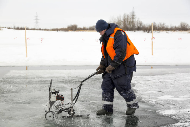 Εργαζόμενος κόβει κομμάτια πάγου σε μέγεθος στον πάγο μιας παγωμένης λίμνης - Φωτογραφία, εικόνα